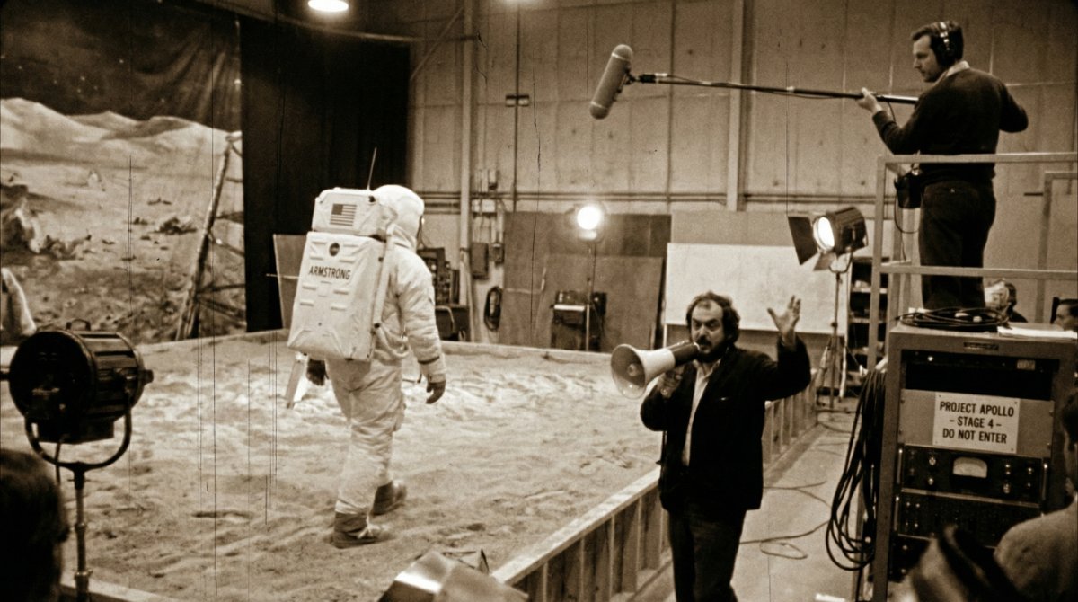 Leaked 1969-style production footage shows Neil Armstrong walking on a staged “Moon surface” before the camera pulls back to reveal a sandbox set, studio lights, and crew in frame. Shot with handheld movement, film grain, and slight blur for an authentic behind-the-scenes look.