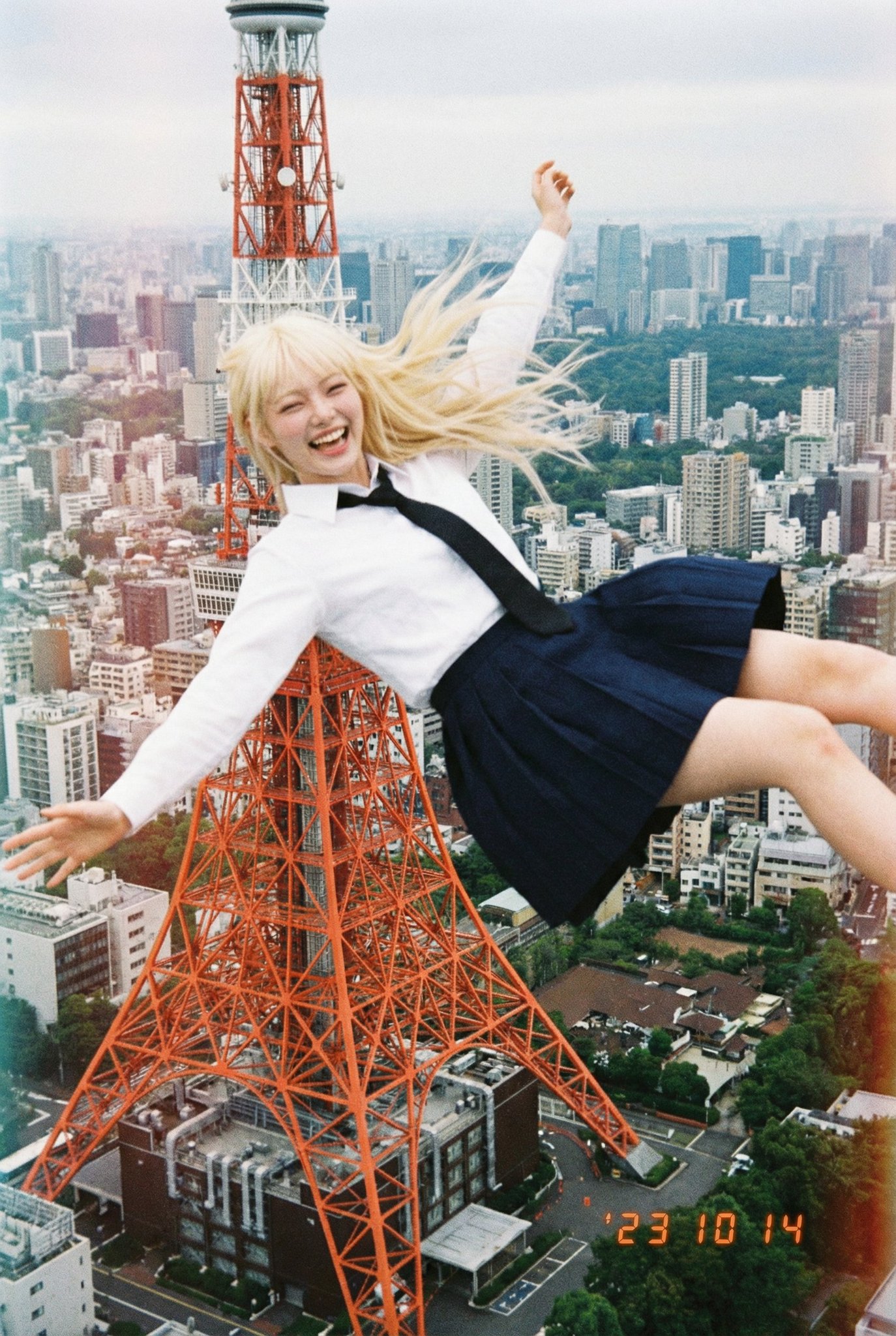 Generate an aerial image that blends seamlessly into the sky above the specified GPS coordinates, with a happy, smiling person integrated as if falling from that exact location. Styled as an ordinary, rough low-resolution disposable-camera snapshot taken by a Japanese high school student.