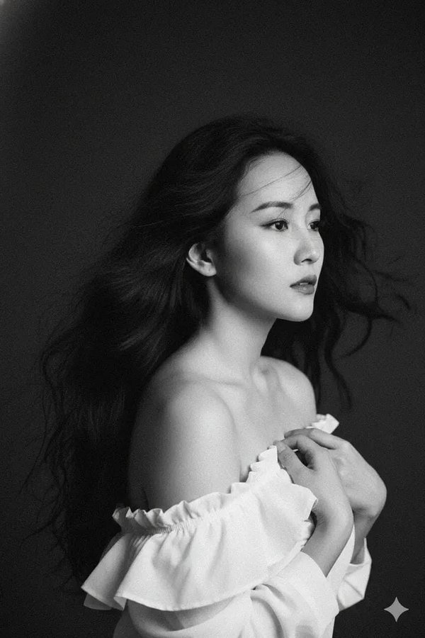 Create a highly artistic 1990s-style monochrome portrait of a beautiful woman with wind-blown wavy black hair, off-shoulder white fabric, and a dark minimalist background, rendered with pronounced 35mm film grain and soft cinematic lighting.
