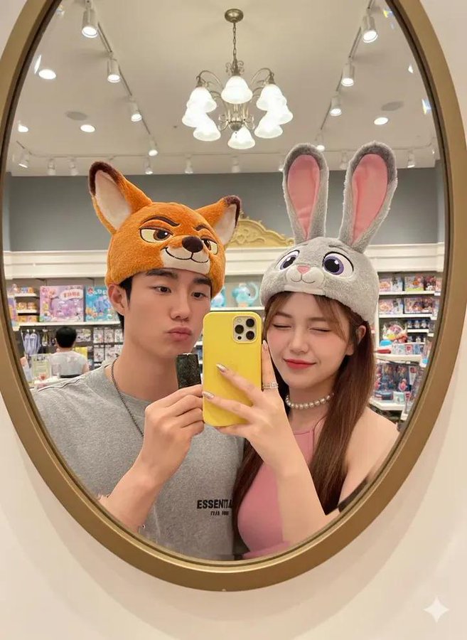 Create a photorealistic 8K oval-mirror selfie of a couple in a Disney gift shop, wearing oversized plush Zootropolis character hats with crisp facial focus and vibrant mall lighting.